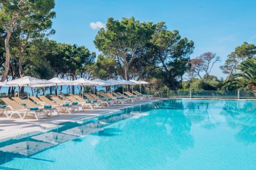 una piscina con tumbonas y sombrillas en Iberostar Club Cala Barca All Inclusive, en Portopetro