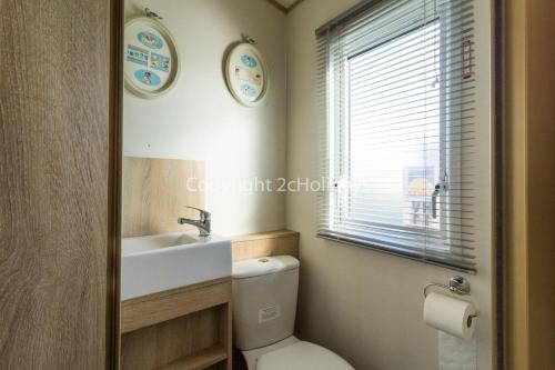 a bathroom with a toilet and a sink and a window at 6 Berth Caravan For Hire At Seawick Holiday Park By The Beach Ref 27011hv in Clacton-on-Sea