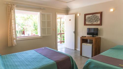 a bedroom with two beds and a television and a window at Pousada Tartaruga in Búzios