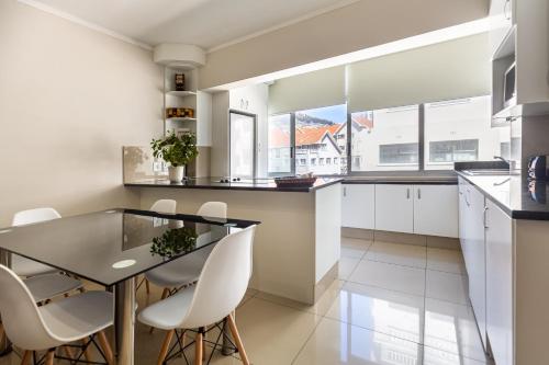 cocina con mesa de cristal y sillas blancas en Perfect Beachfront Apartments, en Ciudad del Cabo