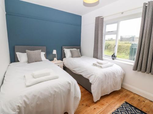 two beds in a room with blue walls and a window at Angorfa in Pwllheli