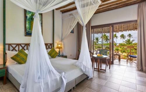 a bedroom with a bed with mosquito nets and a table at Zanzibar Queen Hotel in Matemwe