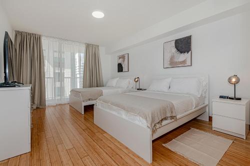 a white bedroom with two beds and a television at Lovely condo with city & ocean views. Sleep up to 6 people! in Miami