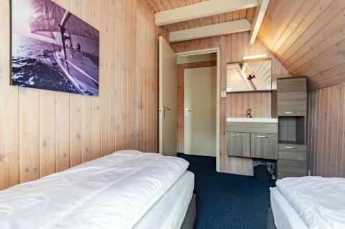 two beds in a room with wooden walls and a sink at Terschelling Natuurlijk in Kinnum