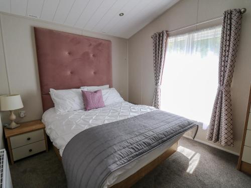a bedroom with a bed with a pink headboard and a window at Ystwyth 36 in Borth