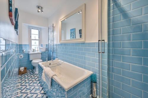 a blue tiled bathroom with a tub and a toilet at The Town House at Muntham- Luxury Holiday Home with Hot Tub in Torquay
