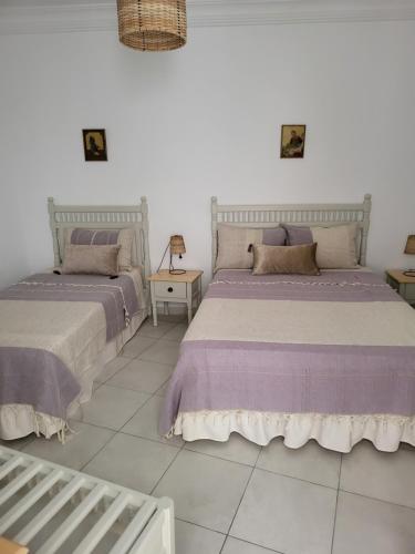 two beds in a white room with purple sheets at Hotel Dar Al Madina in Mahdia
