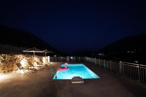 a swimming pool at night with chairs and an umbrella at Villa Tzekos in Kendrokhórion