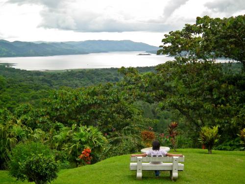 a person sitting on a bench looking out at a lake at Arenal Observatory Lodge & Trails in Fortuna