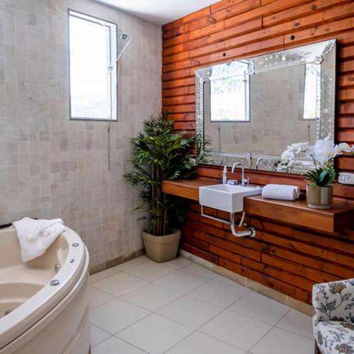 a bathroom with a tub and a sink and a mirror at Bliss Hotel Vale do Café in Vassouras