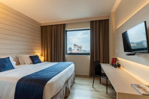 a hotel room with a bed and a desk and a window at Hotel Contemporâneo - Royal Palm Hotels & Resorts in Campinas