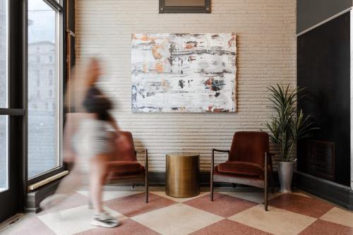 a person walking in a lobby with chairs and a painting at Sonder The Atlee in San Antonio
