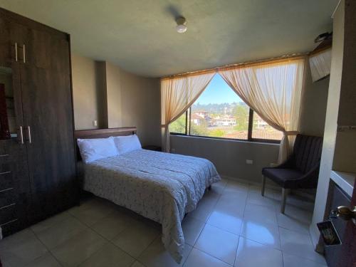 ein Schlafzimmer mit einem Bett, einem Fenster und einem Stuhl in der Unterkunft Hostal el Paraíso in Cuenca