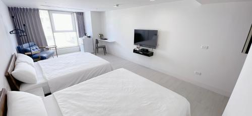 Dieses weiße Zimmer verfügt über 2 Betten und einen TV. in der Unterkunft 三弄旅宿3rd Alley Inn in Kaohsiung