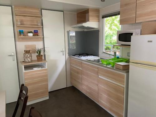 une cuisine avec des armoires en bois et un réfrigérateur blanc dans l'établissement MOBIL HOME Climatisé G058, à Aureilhan