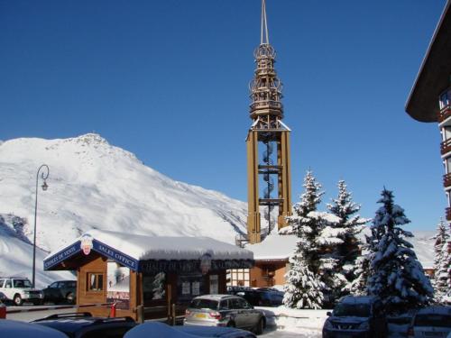 um edifício com uma torre de relógio com uma montanha coberta de neve em Necou 721 em Les Menuires