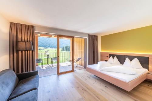 a bedroom with a bed and a couch and a balcony at Hotel Tyrol in Valle Di Casies