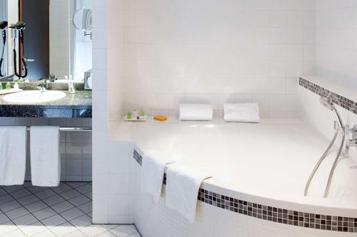 a white bathroom with a tub and a sink at NH Wien City in Vienna