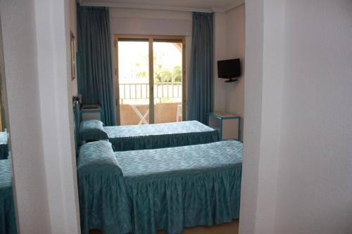 three beds in a room with a window at Hotel Playa Grande in Puerto de Mazarrón