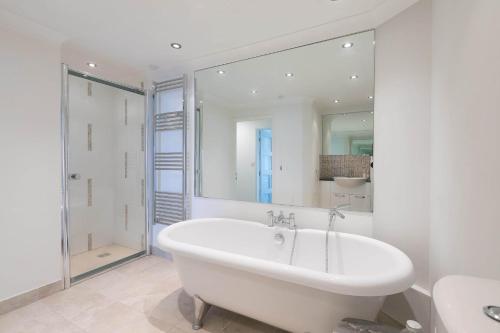 a white bathroom with a large mirror and a tub at Golden Heights in Carbis Bay