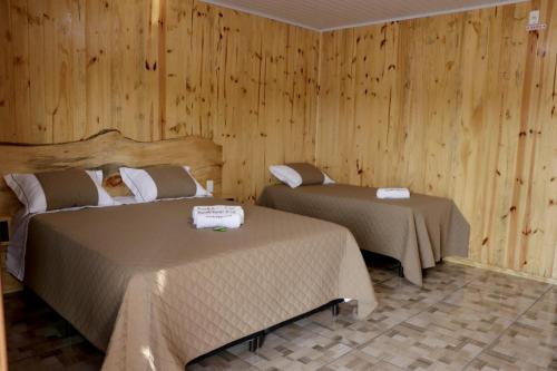 two beds in a room with wooden walls at Pousada Refúgio do Sol in Cambara do Sul