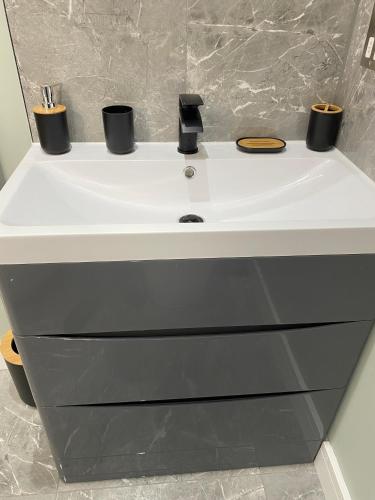 a white bathroom sink with black cups on it at Stylish 2 Bed Apt, 2 Minute Walk From The Beach. in Sheringham