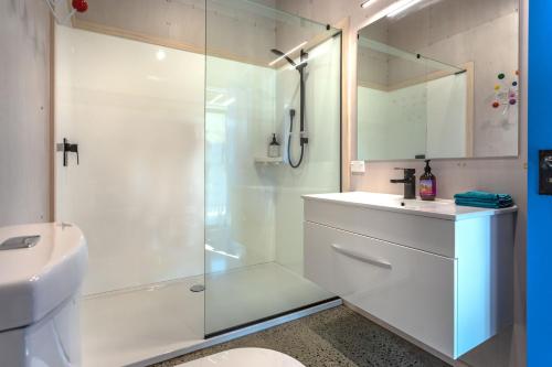 a white bathroom with a shower and a sink at Hahei Beach Bach. in Hahei