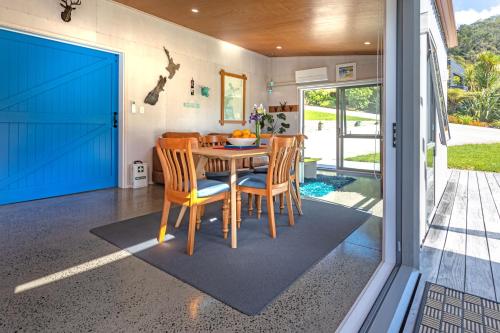 a dining room with a table and chairs and a blue door at Hahei Beach Bach. in Hahei