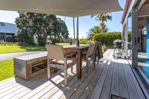a wooden deck with a table and chairs and an umbrella at Hahei Beach Bach. in Hahei