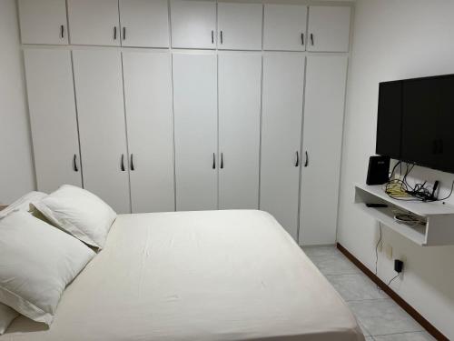 ein weißes Schlafzimmer mit Bett und Flachbildfernseher in der Unterkunft Casa beira mar cond fechado farol Itapuã in Salvador
