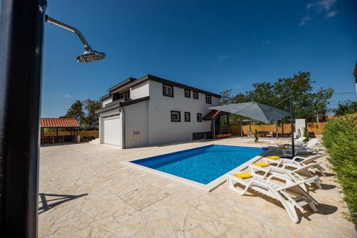a swimming pool with chairs and an umbrella and a house at Villa Heaven in Donji Zemunik