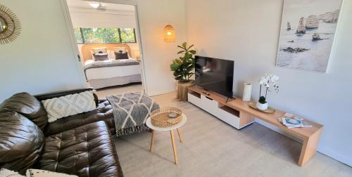 Noosa River Retreat Apartments - Perfect for Couples & Business Travel في نوسافيل: غرفة معيشة مع أريكة جلدية وتلفزيون