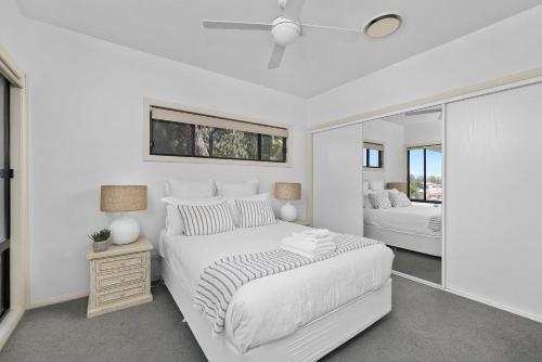 a white bedroom with a bed and a mirror at Wanda Point House - pure tranquillity and walk to beach in Salamander Bay