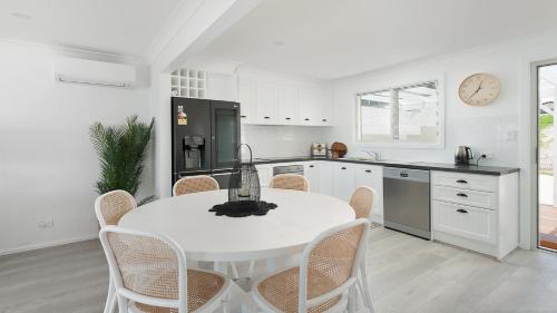 a white kitchen with a white table and chairs at The Beach Shack on Wanda - Waterfront Coastal Chic in Salamander Bay