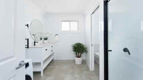 ein Badezimmer mit einem Waschbecken, einem WC und einem Spiegel in der Unterkunft The Beach Shack on Wanda - Brand New Beachfront Luxury in Salamander Bay