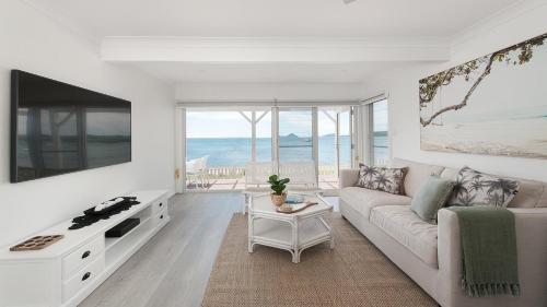 a white living room with a couch and a tv at The Beach Shack on Wanda - Waterfront Coastal Chic in Salamander Bay