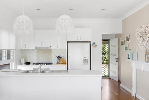 a white kitchen with white cabinets and a sink at Fingal Bay Beach House - Water Views and Seconds From the Beach in Fingal Bay