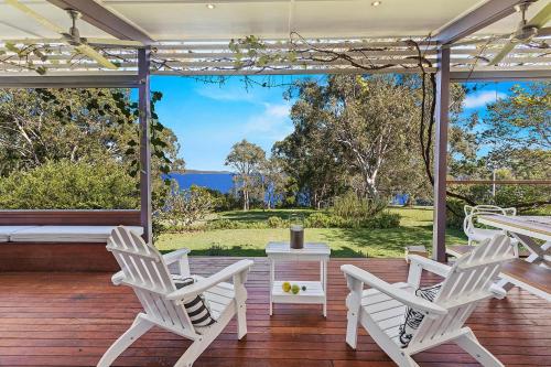 a porch with white chairs and a table and a view of the ocean at Driftwood in Soldiers Point