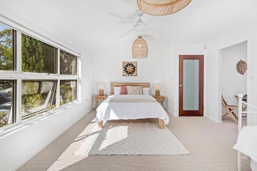 a white bedroom with a bed and windows at Driftwood in Soldiers Point