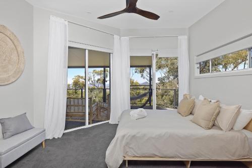 a white bedroom with a bed and a couch and windows at Seascape Retreat - Magnificent 5 Bedroom Home in Nelson Bay