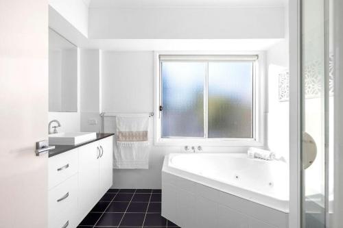 a white bathroom with a tub and a window at The Home Resort - One Mile Beach in One Mile