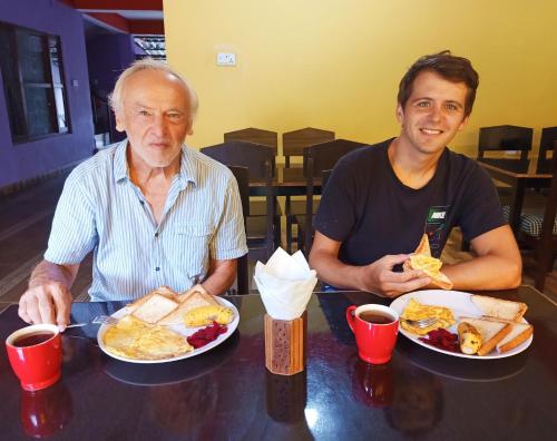 Dois homens sentados numa mesa com pratos de comida. em Hotel Rhinoceros-Homestay em Sauraha