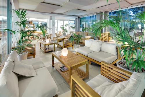 a restaurant with white couches and tables and plants at Hotel Europa Lignano in Lignano Sabbiadoro