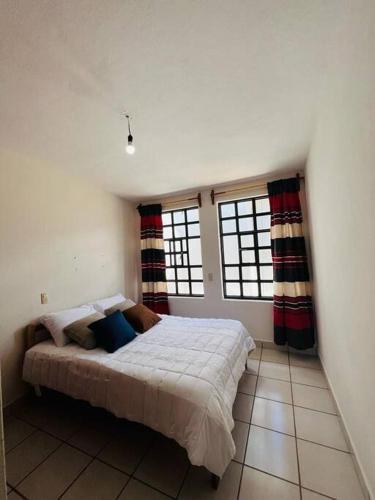 a bedroom with a bed in a room with two windows at Amplio Dpto. céntrico con cochera y terraza. in San Cristóbal de Las Casas