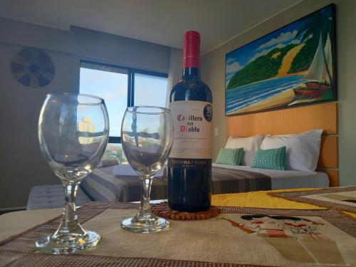 a bottle of wine and two wine glasses on a table at Ilusion Flats Aconchego de Ponta Negra in Natal