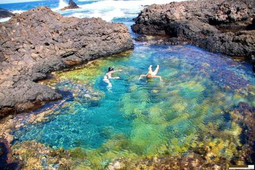 two people swimming in a body of water with rocks at FARINHA DE PAU - ECO B&B in Tarrafal