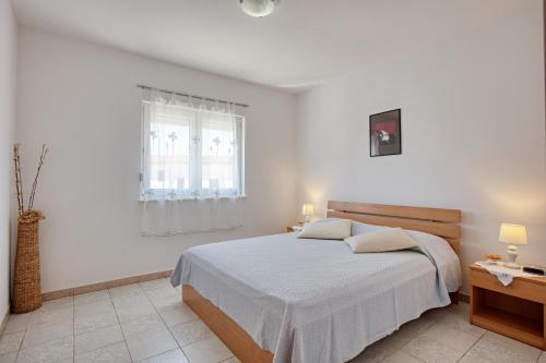 a white bedroom with a bed and a window at Apartments by the sea Rogoznica - 19367 in Rogoznica