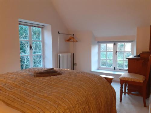 a bedroom with a large bed and two windows at Characterful Cottage adjacent to an Orchard in Brockley