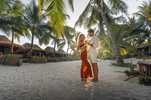 a man and woman standing on a beach with palm trees at Villa Pescadores Tulum in Tulum