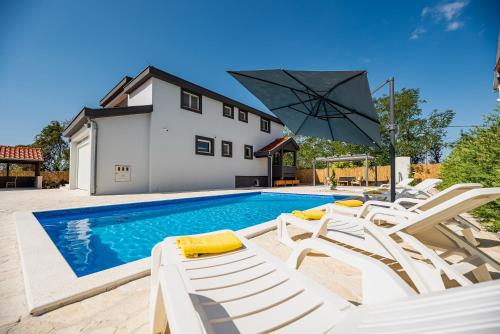 a swimming pool with white chairs and an umbrella at Villa Heaven in Donji Zemunik